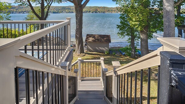 A wooden staircase leading to a deck overlooking a lake, with a small shed and trees in the background. - Fun in the Sun - Walk Into Town on Keuka's East Side (Penn Yan)