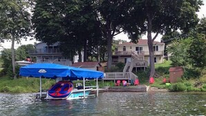 A lake with a dock, a covered boat, and a house with a deck and stairs. - Fun in the Sun - Walk Into Town on Keuka's East Side (Penn Yan)