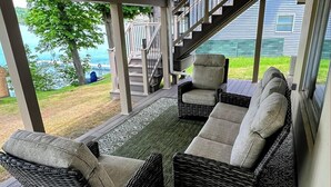 A covered outdoor seating area with wicker furniture and a patterned rug, overlooking a backyard and a staircase. - Fun in the Sun - Walk Into Town on Keuka's East Side (Penn Yan)