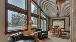 Una sala de estar acogedora con sofás de cuero, una mesa de comedor y grandes ventanales con vistas a árboles cubiertos de nieve.