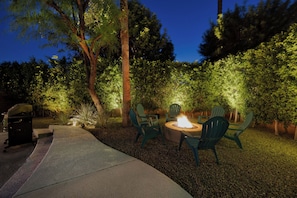 An outdoor patio with a fire pit, green chairs, and a grill.