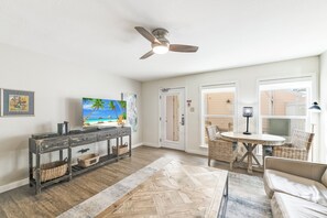 A living room with a television, a ceiling fan, wicker furniture, and a herringbone-patterned rug.
