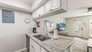 A kitchen with a double sink, white cabinets, a clock, and a fire extinguisher. - Chic Poolside Condo | Ultimate Beachfront Escape (Corpus Christi)