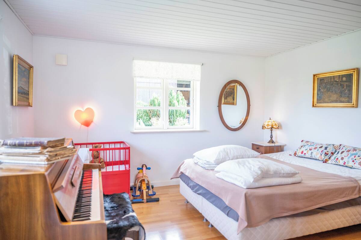 Un dormitorio con cama, piano, ventana y espejo.