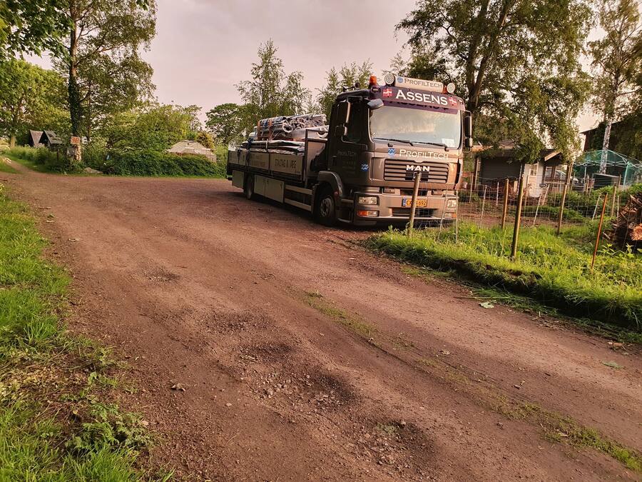 A truck parked on a dirt road with greenery on both sides.