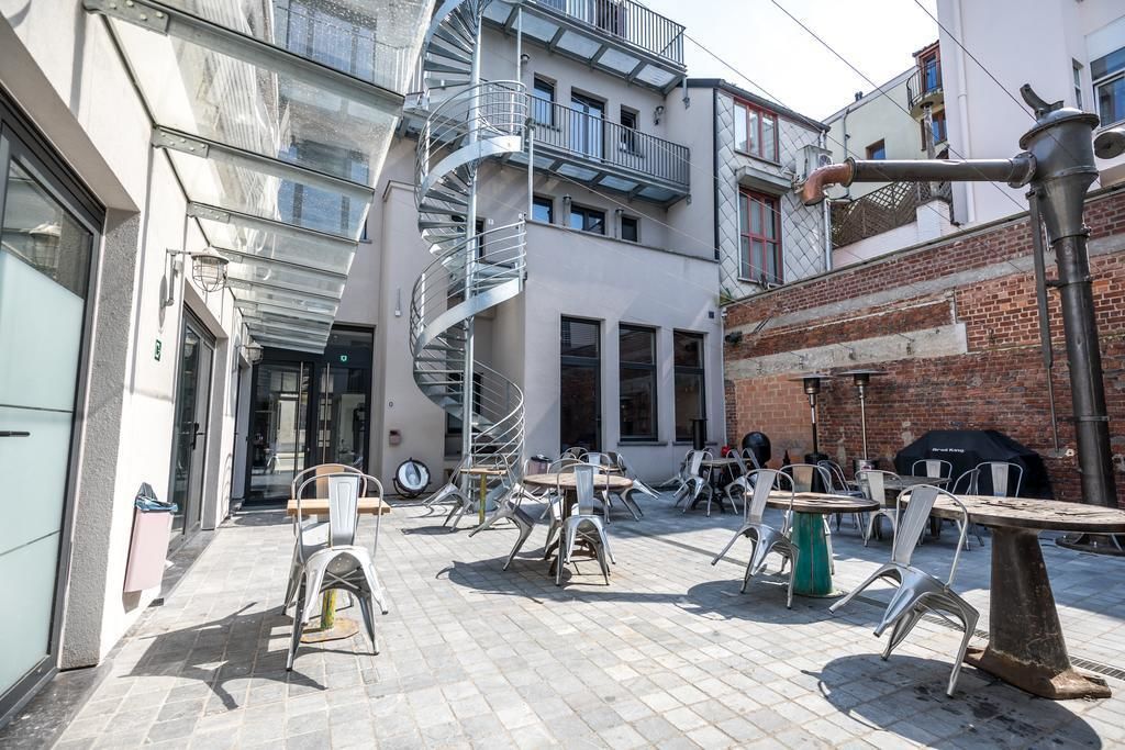 An outdoor cafe area with multiple tables and chairs, a spiral staircase, and a brick wall.