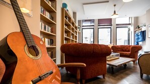 Una sala de estar con una guitarra, estanterías, un sofá rojo y una mesa de centro de madera.