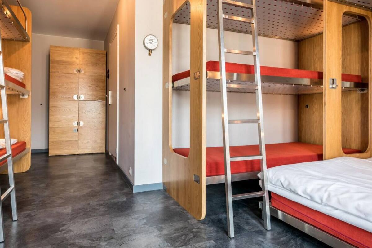Une chambre avec des lits superposés, des échelles en métal, des portes en bois et une horloge au mur.