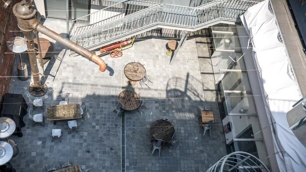 Una terraza exterior con mesas y sillas redondas, una escalera metálica y una gran escultura de metal.