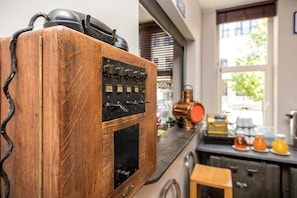 Una radio de madera antigua con perillas y un auricular de teléfono, sobre una encimera de cocina con electrodomésticos modernos y una ventana al fondo.
