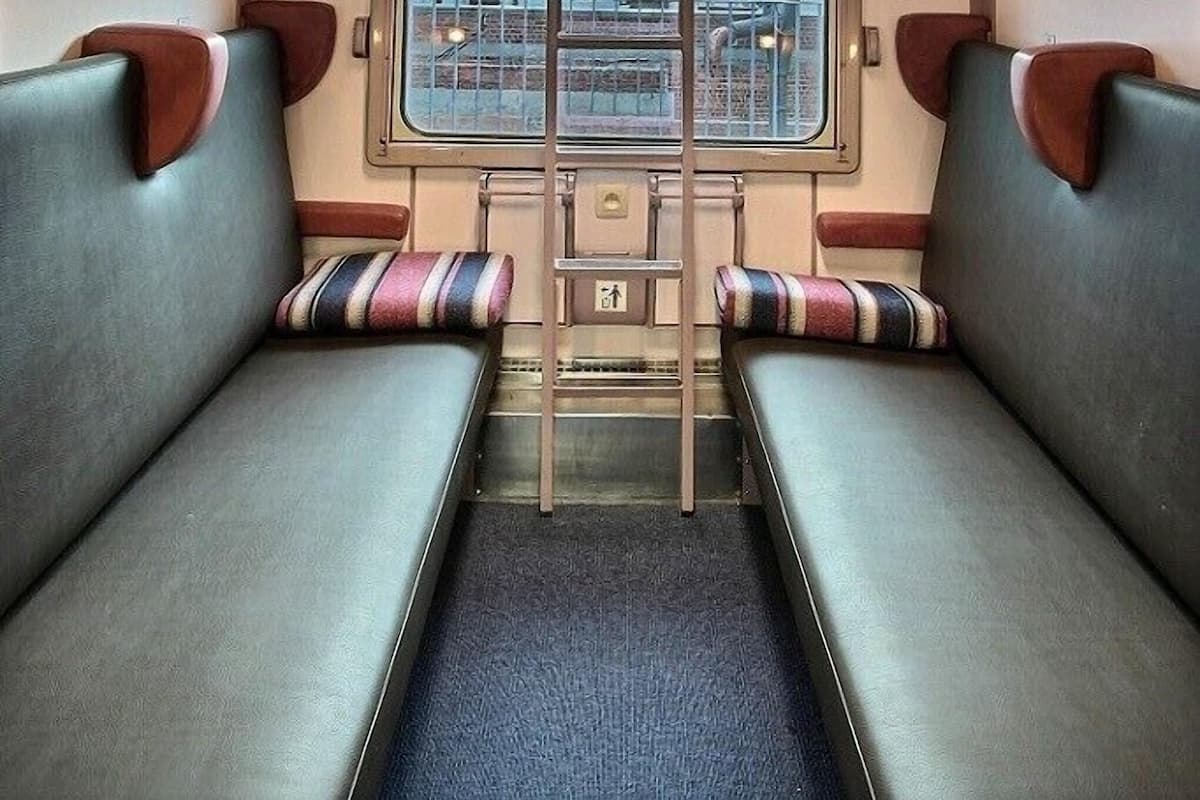 L’intérieur d’un wagon de train, avec une allée centrale, des banquettes de chaque côté et une fenêtre au fond.