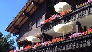Un chalet traditionnel doté de balcons en bois, d’un espace extérieur aménagé pour s’asseoir et d’une voiture garée devant.