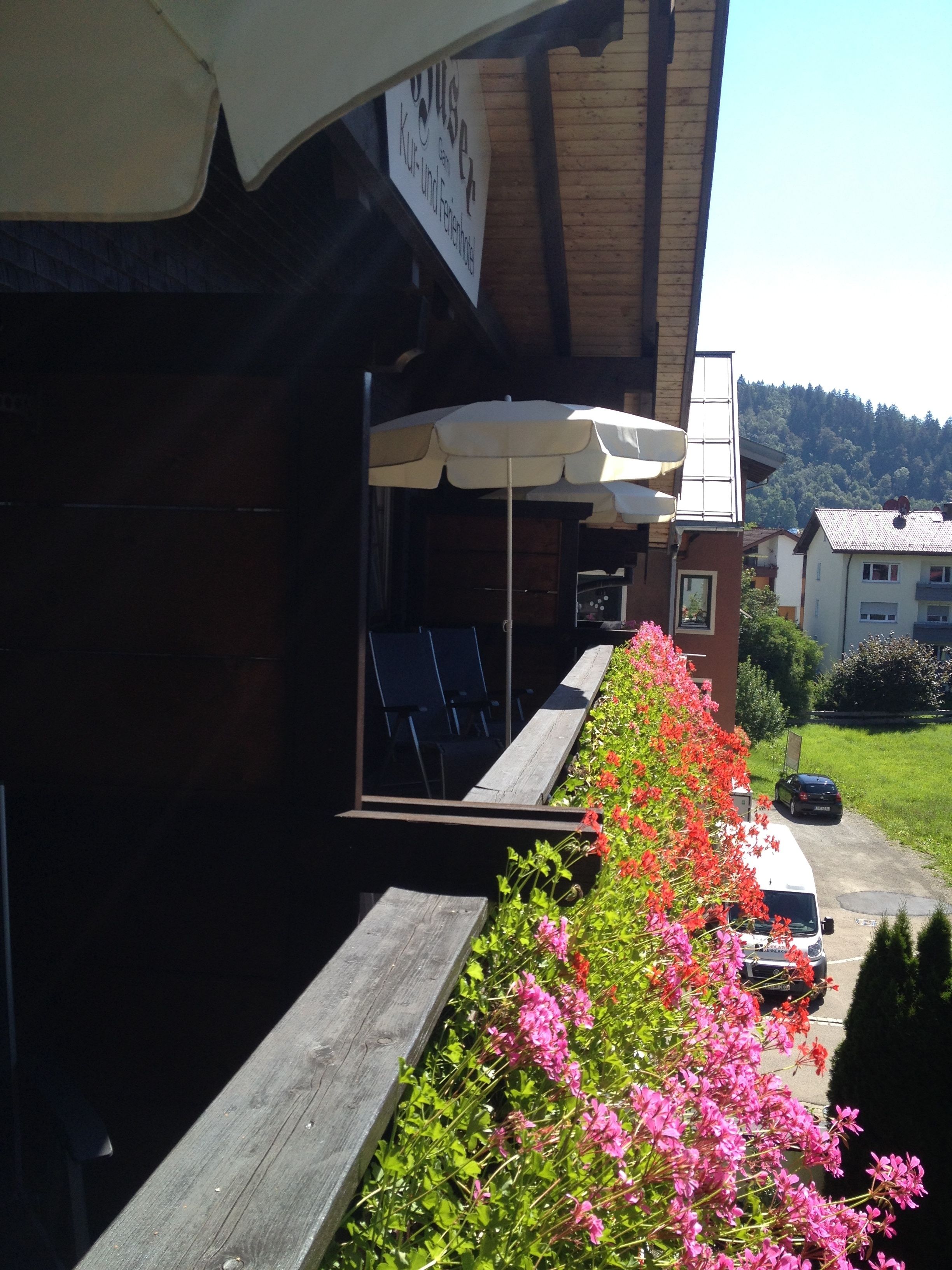 Ein Gebäude mit Außenbestuhlung unter Sonnenschirmen, einer Holzterrasse und einem blumenbepflanzten Weg.
