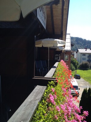 A building with outdoor seating under umbrellas, a wooden deck, and a flower-lined pathway.