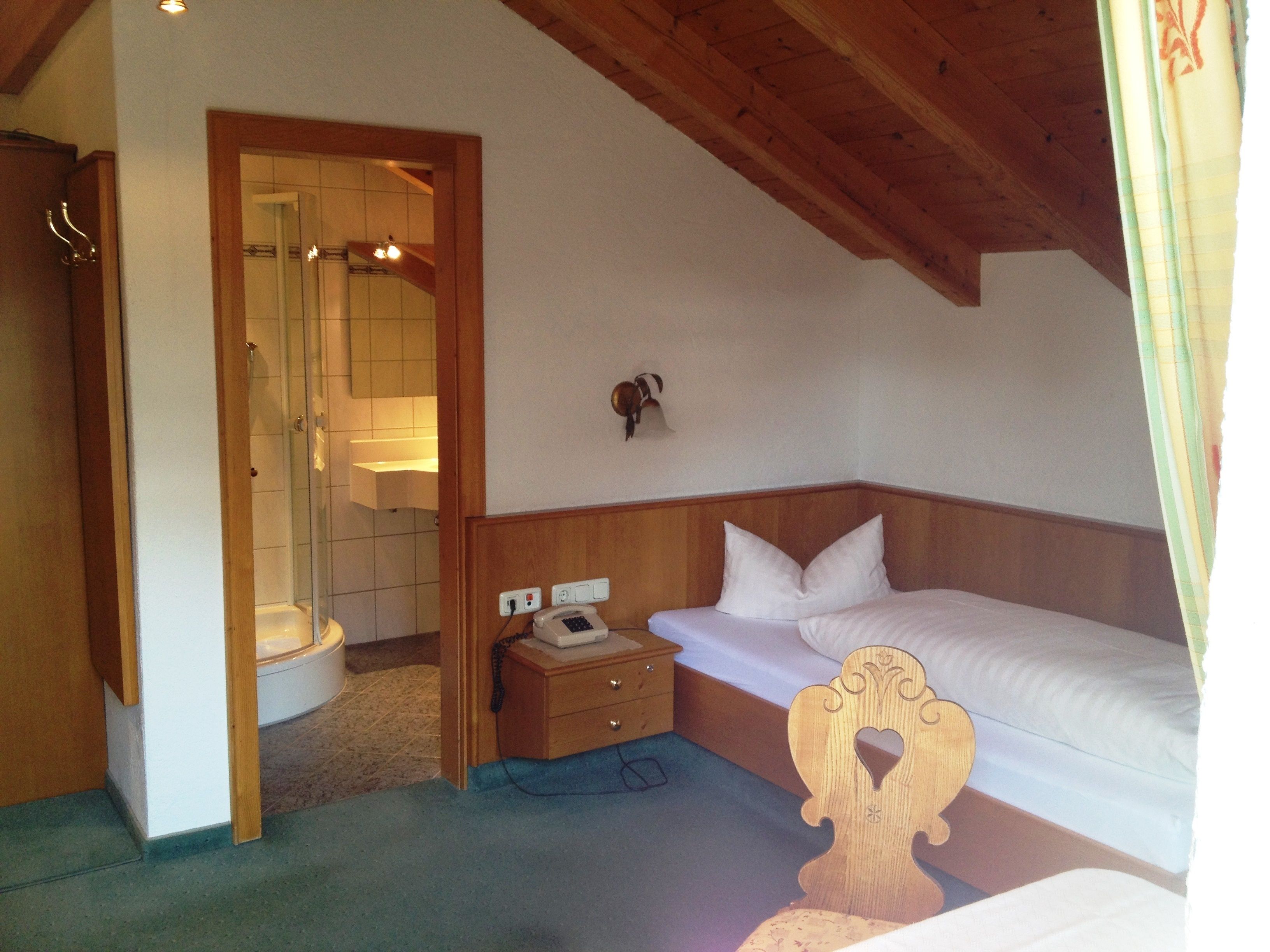 A bedroom with a wooden headboard, a bedside table with a telephone, and a bathroom visible through an open door.