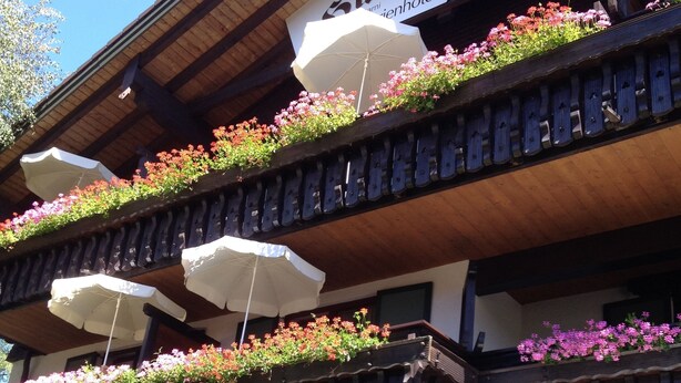 Un hôtel à la façade en bois, doté de balcons ornés de jardinières, d’un espace extérieur aménagé avec des sièges et des parasols.