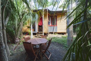 A wooden cabin with a dining area featuring a table and chairs, surrounded by lush greenery.