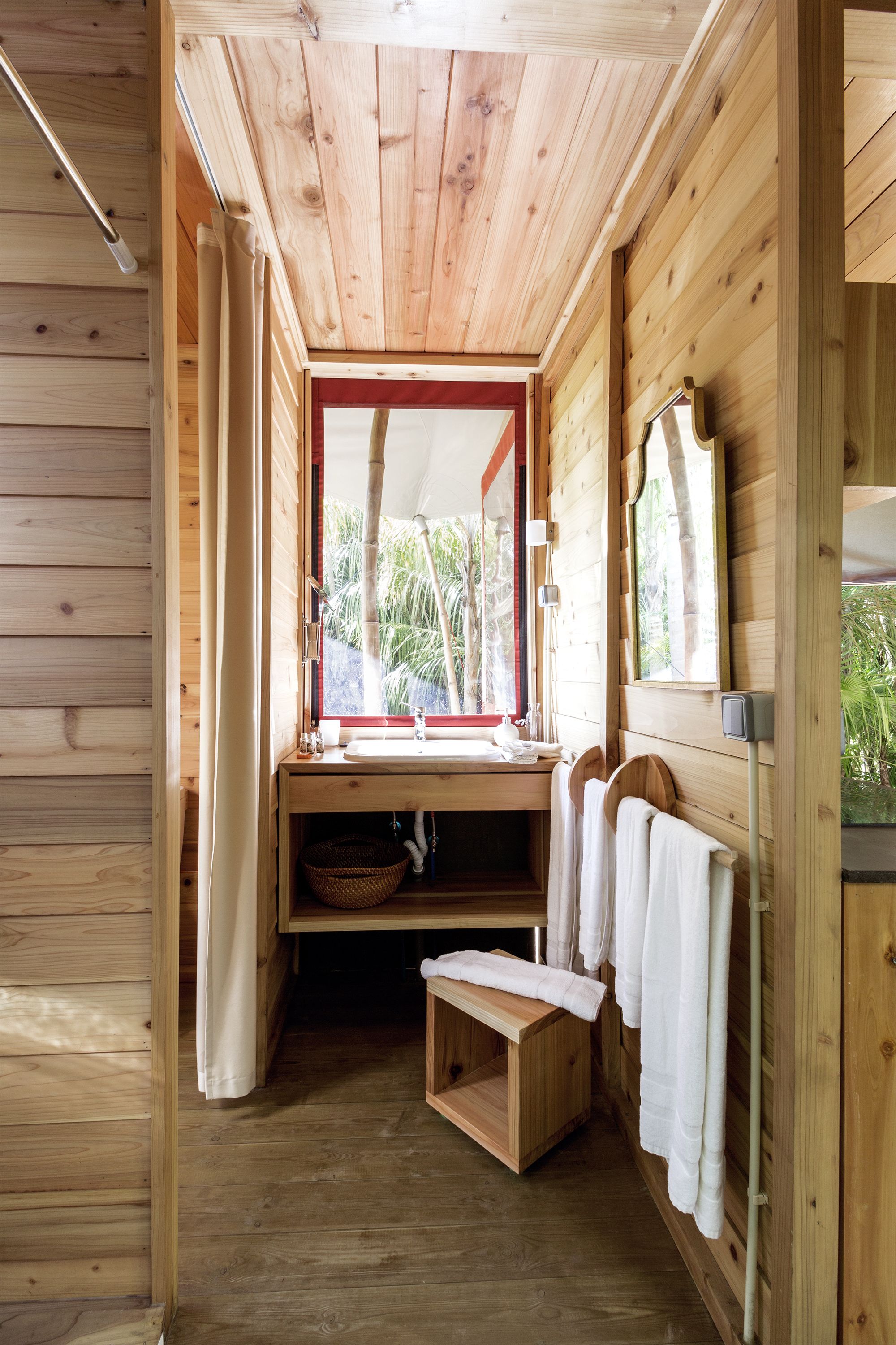 Baño de cabaña de madera con banca de madera, lavabo y espejo.