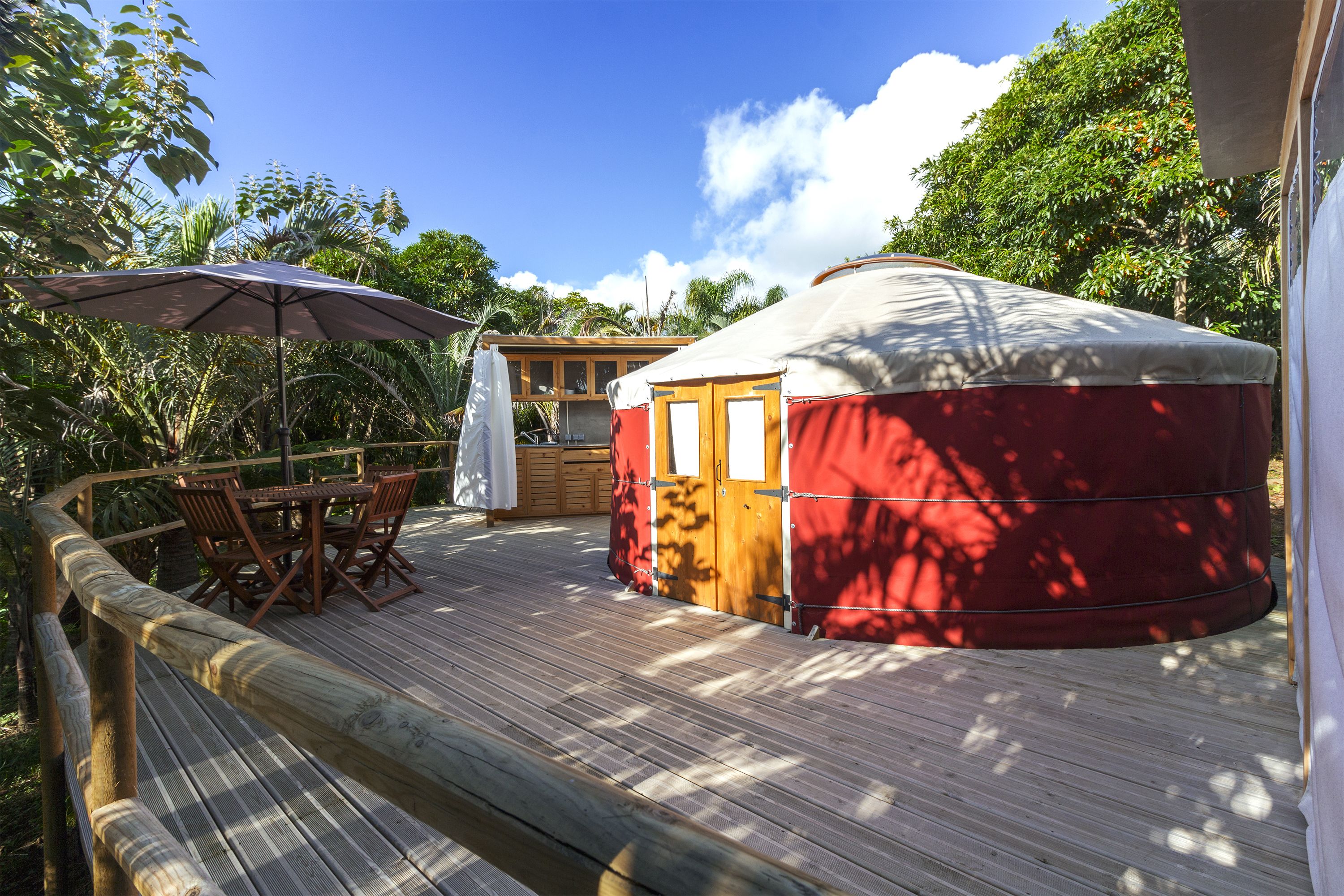 A yurt with a wooden deck, a table with chairs, and a large umbrella.