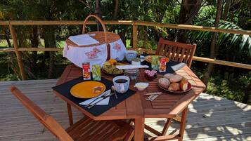 A wooden deck with a table set for breakfast, including bread, fruit, and beverages.