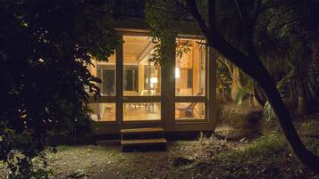 A wooden cabin with glass walls, a staircase leading to the entrance, and a well-lit interior.