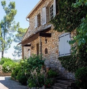 A stone house with a covered porch, surrounded by greenery and trees. - Domaine l'Helion (Taradeau)