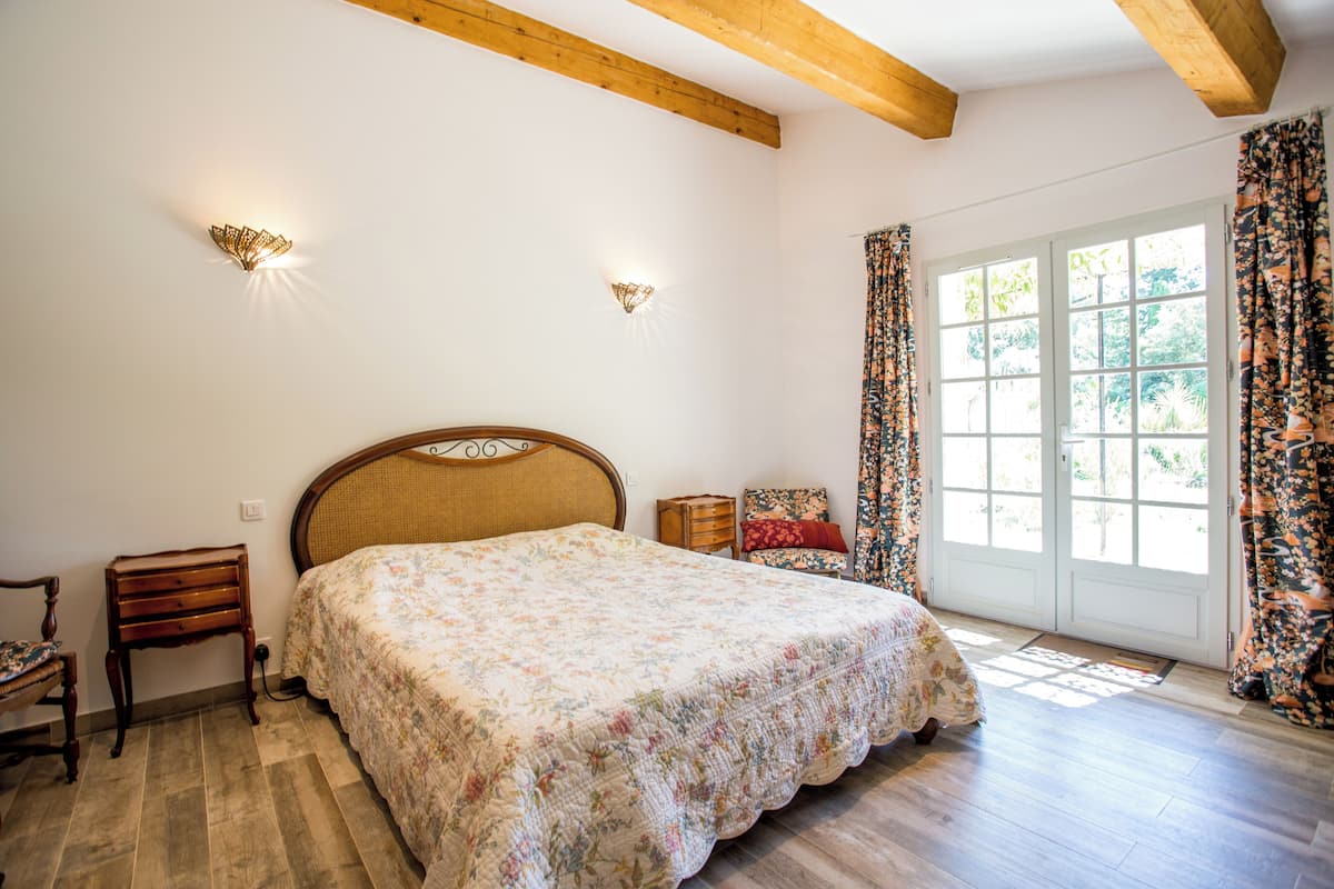 A bedroom with a wooden bed, a nightstand, a chair, and a window with curtains.