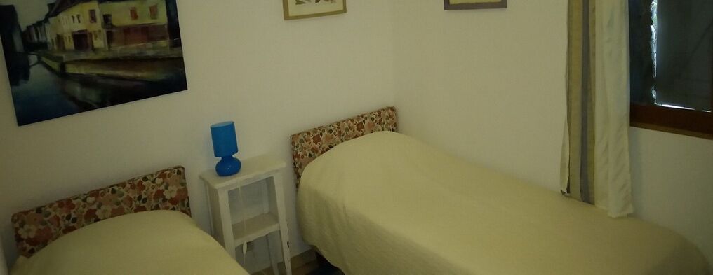 A small room with two beds, a white nightstand, and a painting on the wall.