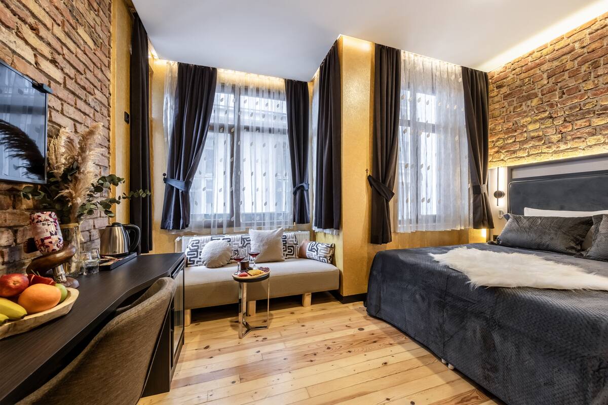 A modern room with a brick wall, a sofa, a bed, and a dining area with fruits and a kettle.