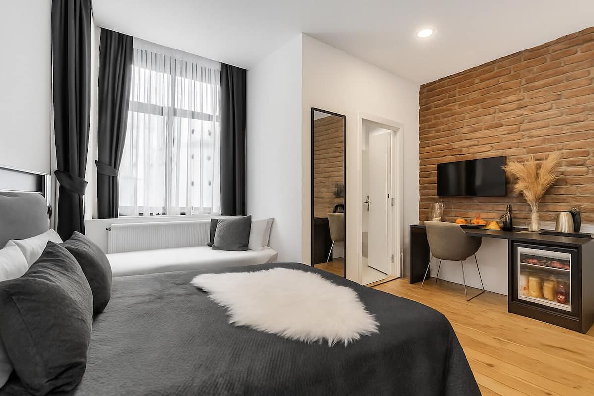 A modern hotel room with a bed, a seating area, a desk with a TV, and a kitchen counter.