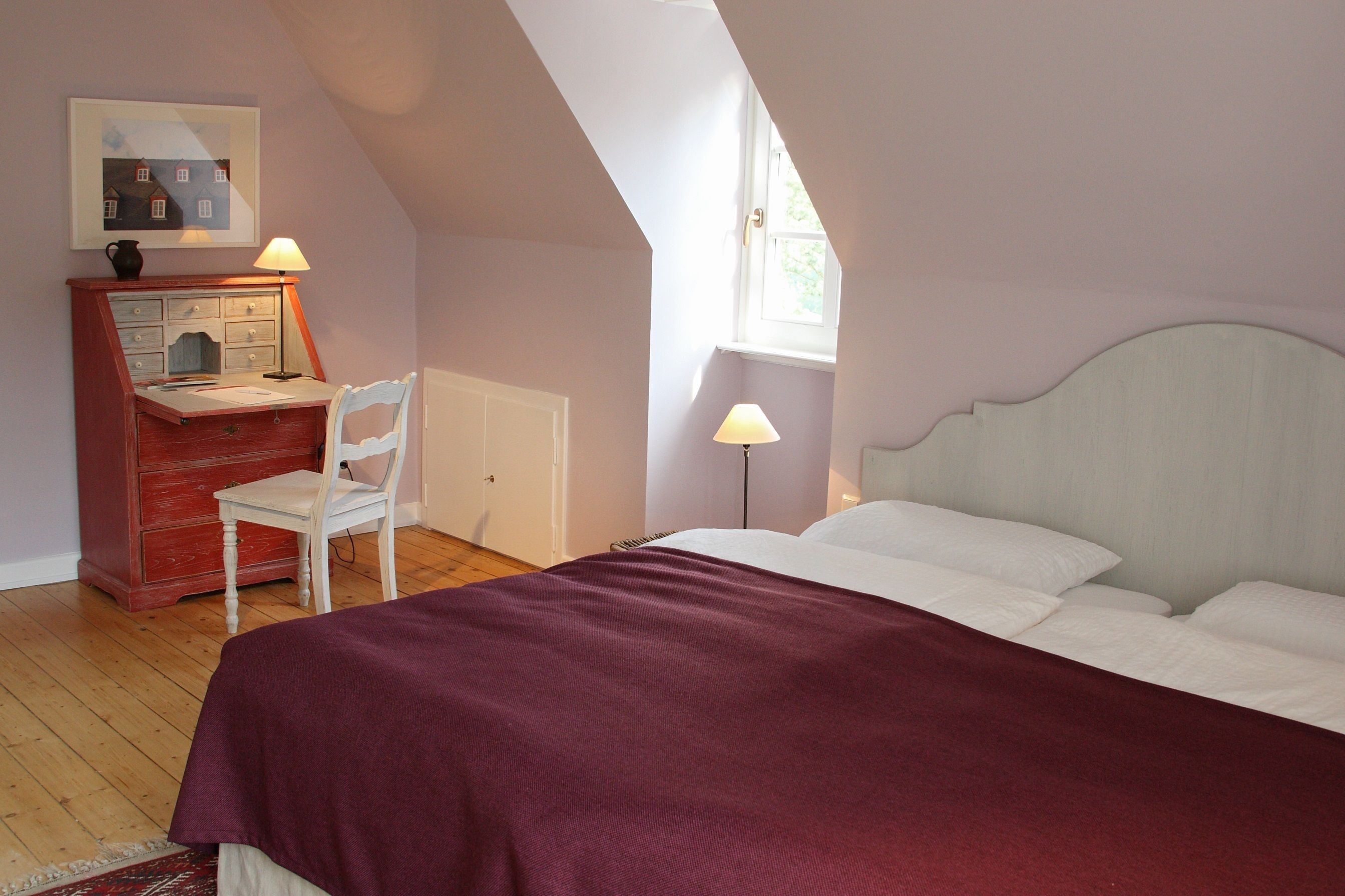 Een slaapkamer met een bed, een bureau met stoel, een lamp en een raam.