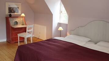 Een slaapkamer met een bed, een bureau met stoel, een lamp en een raam.