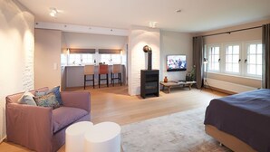 Un salon moderne avec un canapé, un lit, une télévision, une cheminée et un coin cuisine à l’arrière-plan.