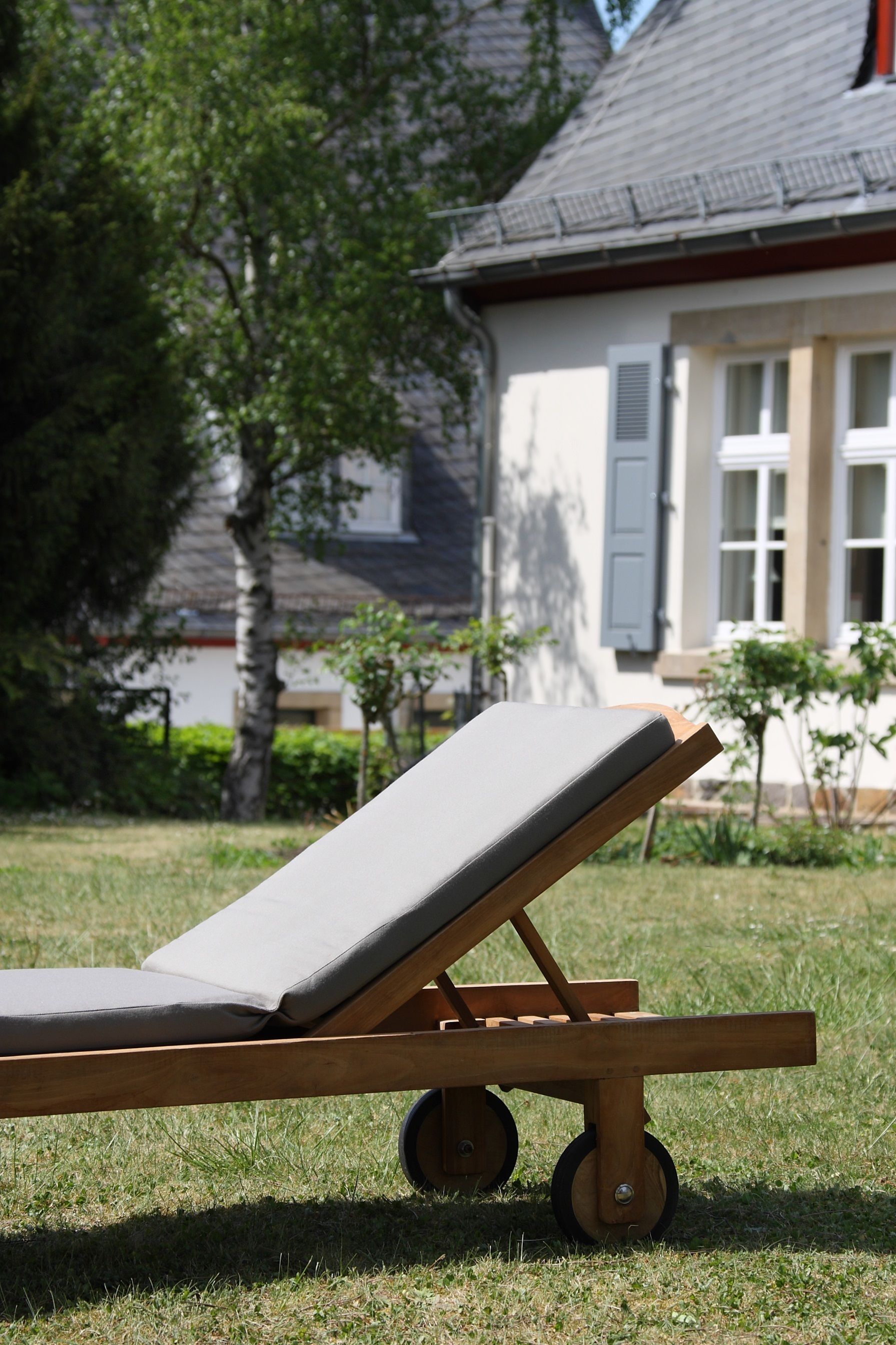 Un fauteuil de jardin en bois, muni de roulettes, posé sur une pelouse.