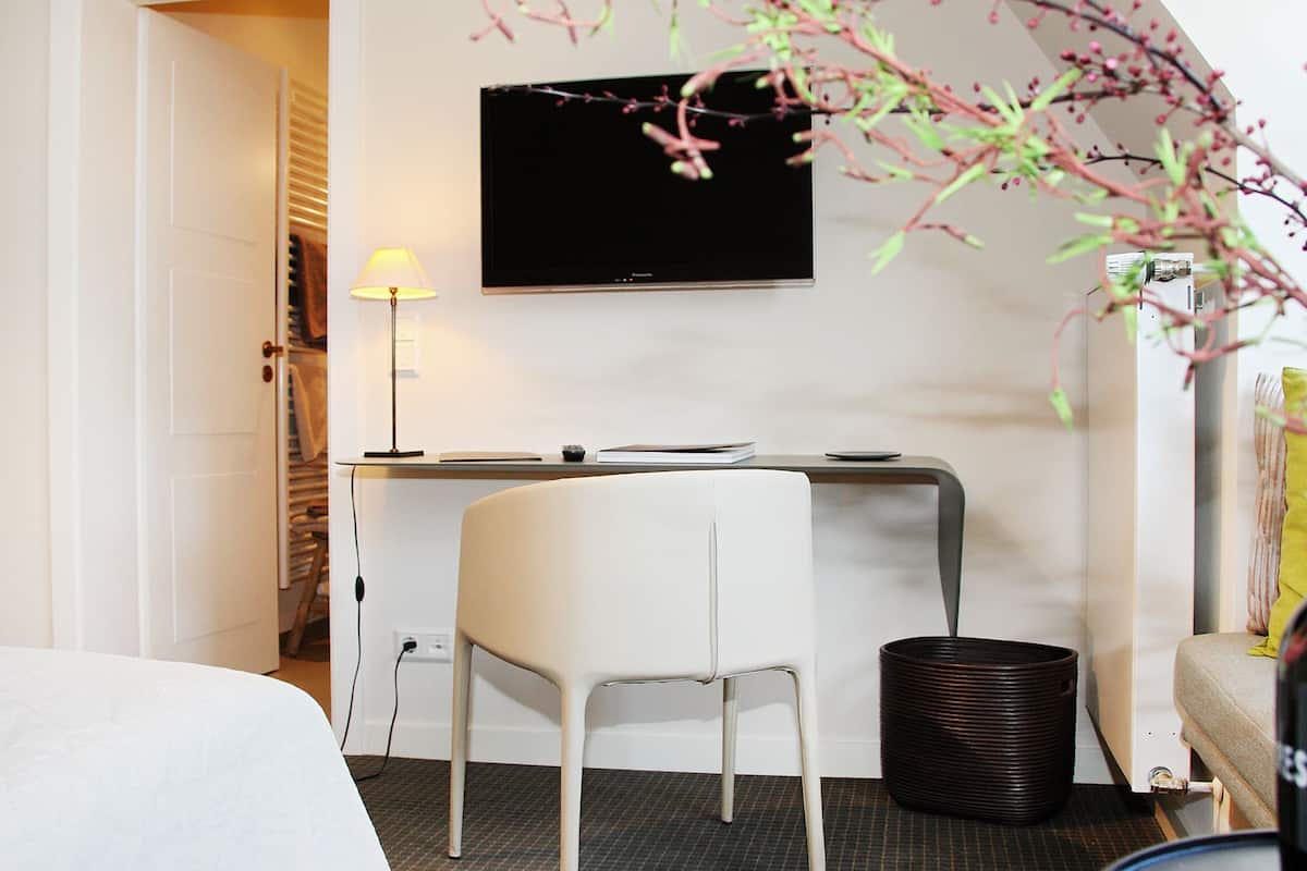 Habitación de hotel con cama, escritorio con computadora, televisor, lámpara y un cesto de basura.