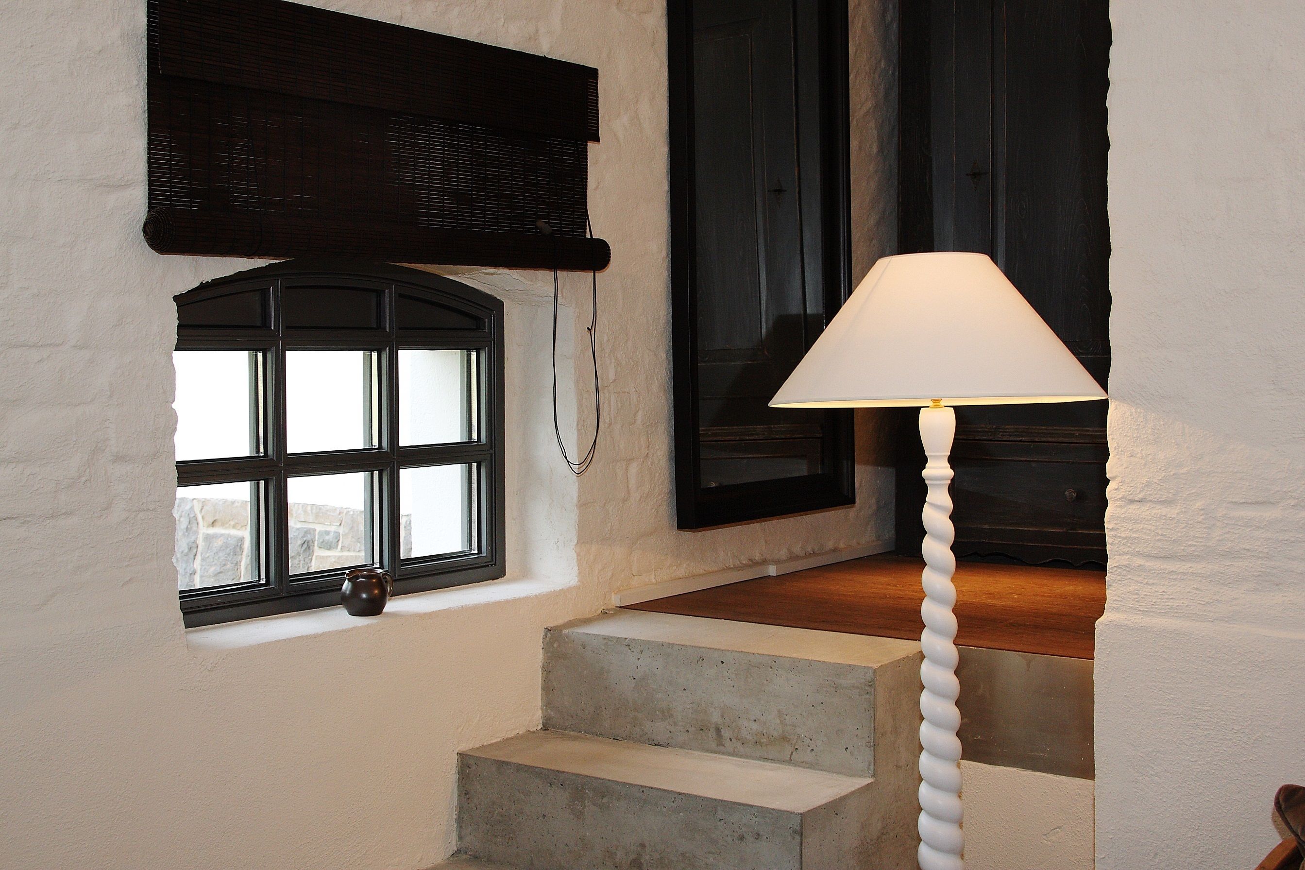 A staircase with a concrete finish, a white wall, and a window with a black frame.