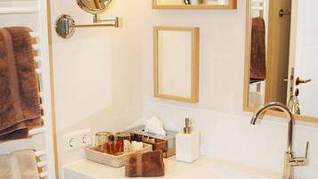 A bathroom with a white sink, a mirror, a towel rack, and a shelf with toiletries.