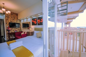 A hotel room with a large bed, a TV, a red sofa, and a balcony with a railing.