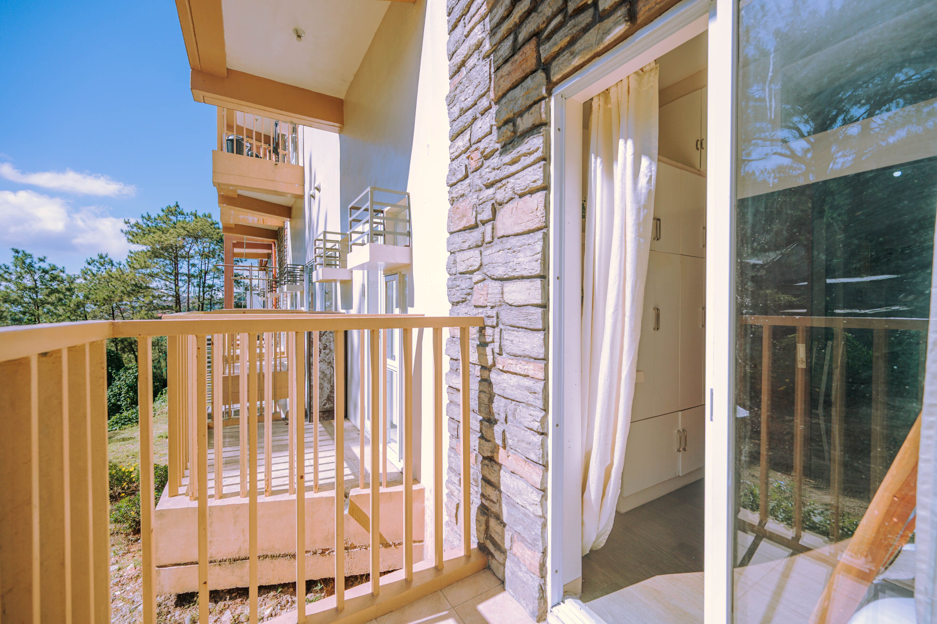A balcony with a stone wall, a wooden railing, and a glass door leading to a room.