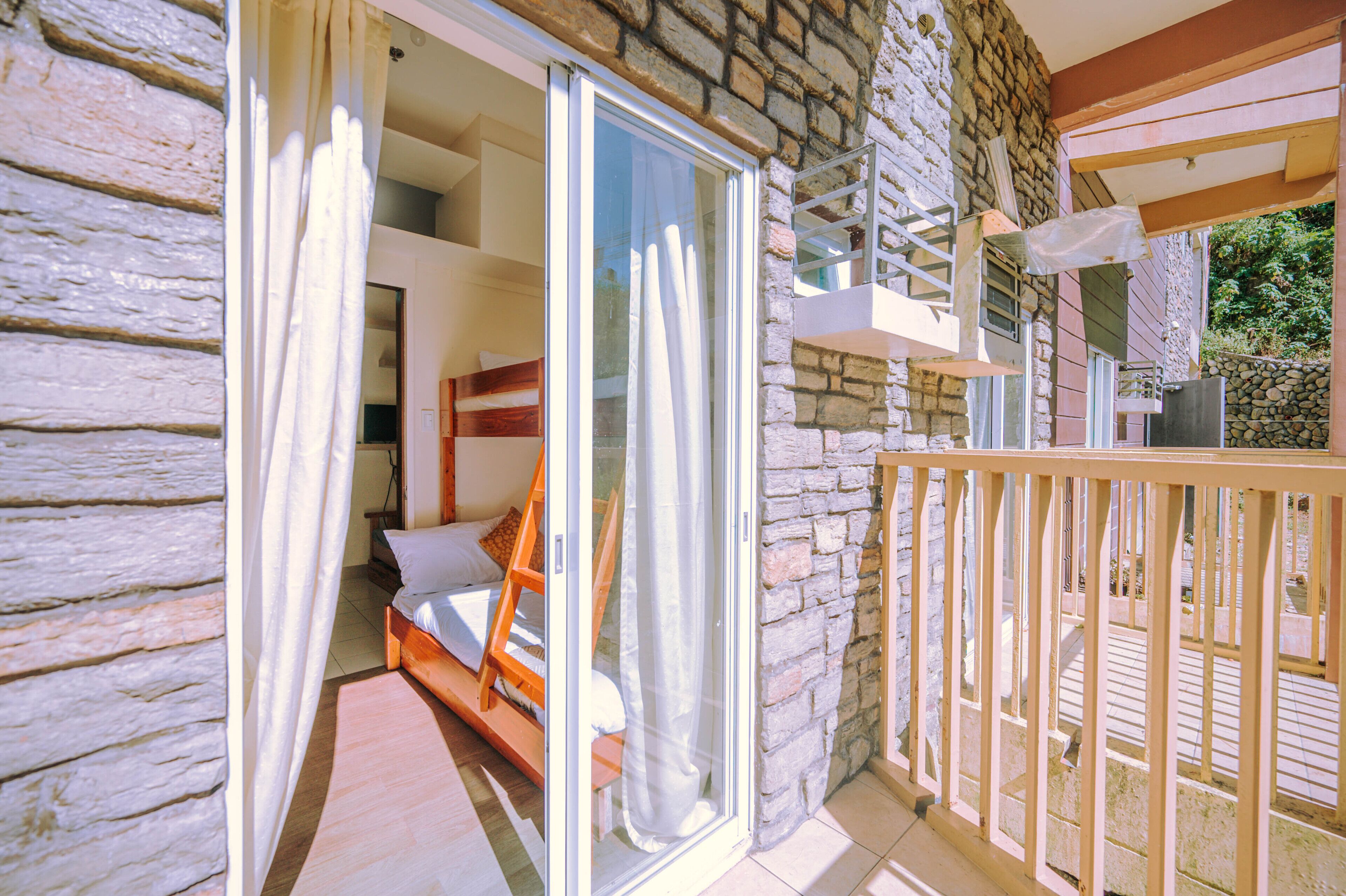 A bedroom with a wooden bed, a sliding glass door leading to a balcony, and stone walls.