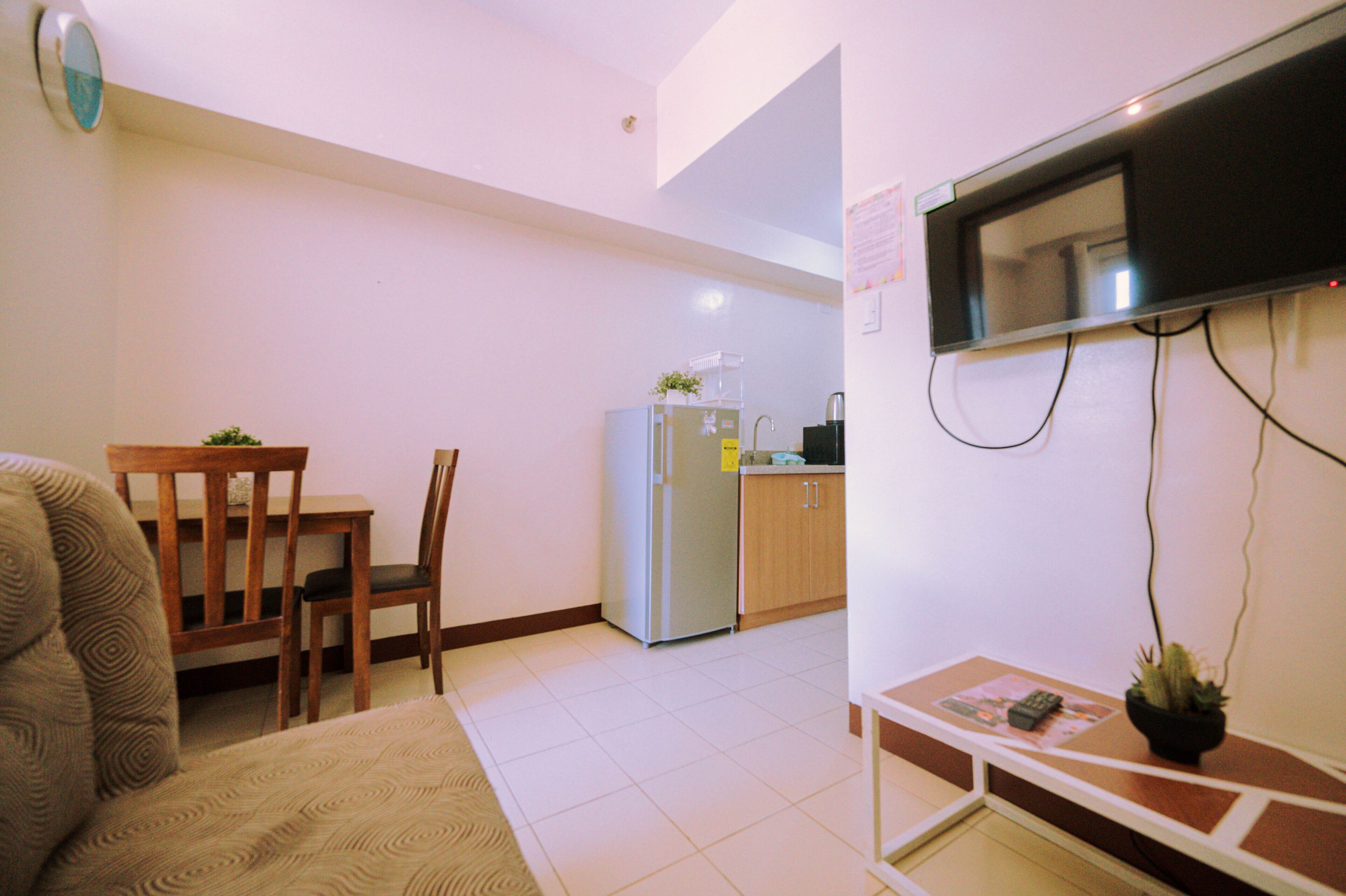 Un espacio habitable compacto con sofá, mesa de comedor con sillas, zona de cocina con refrigerador y televisor montado.