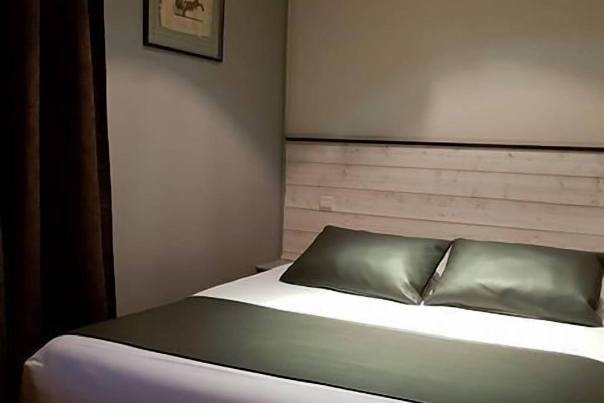 Hotellihuone, jossa on sänky, seinällä kehystetty taulu ja verho.