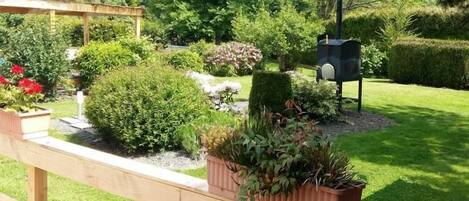 Un banco de madera con plantas en macetas, un buzón y un jardín bien cuidado con diversos arbustos y flores.