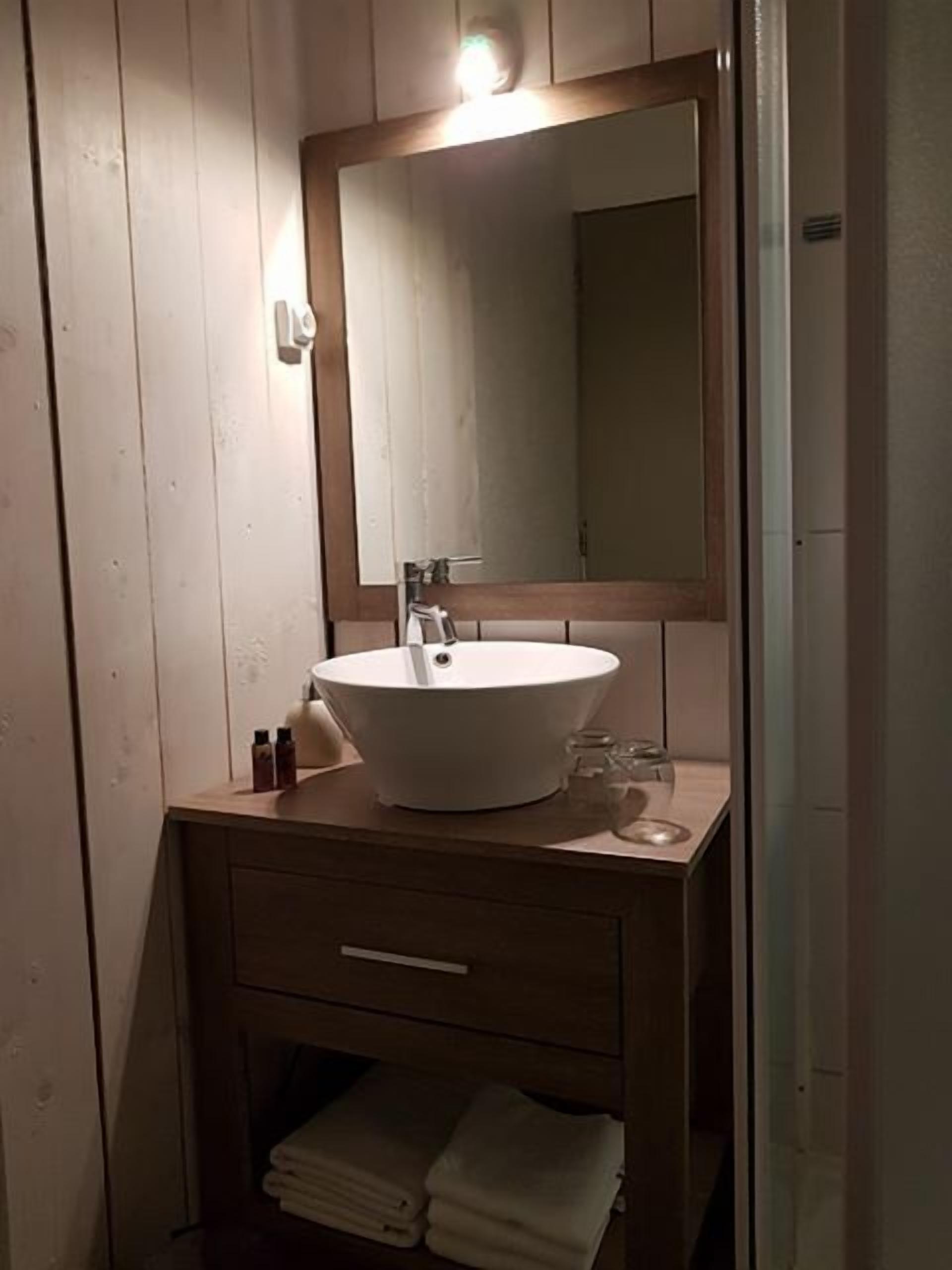 A bathroom with a wooden vanity, a white sink, a mirror, and a towel rack.