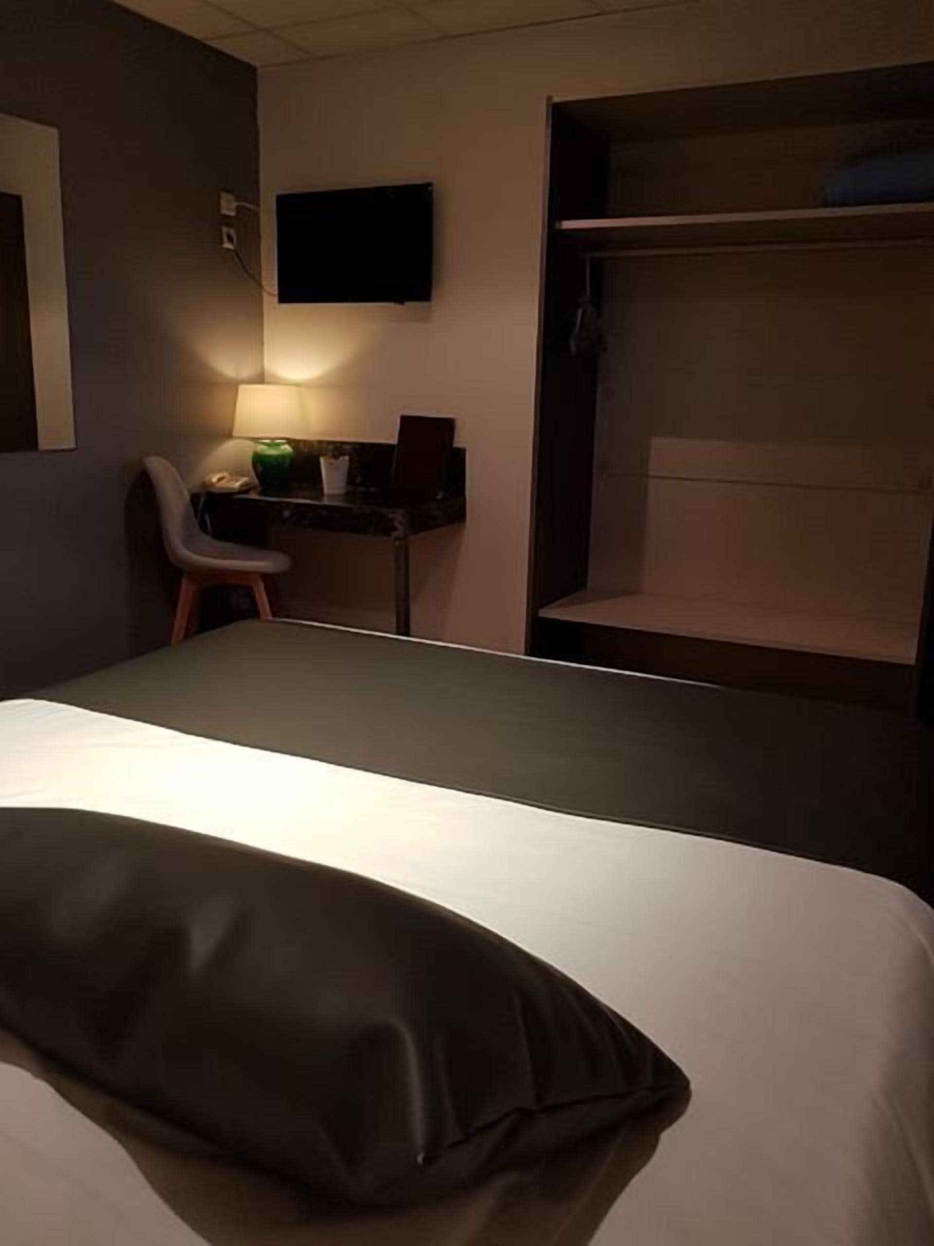 A hotel room with a bed, a desk, a chair, and a TV mounted on the wall.