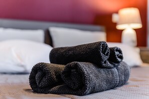 A neatly made bed with rolled towels and a lamp in the background.