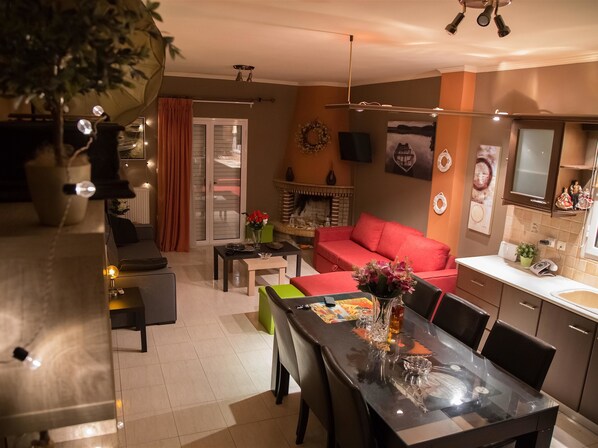 A modern living room with a glass dining table, red sofa, and a fireplace.