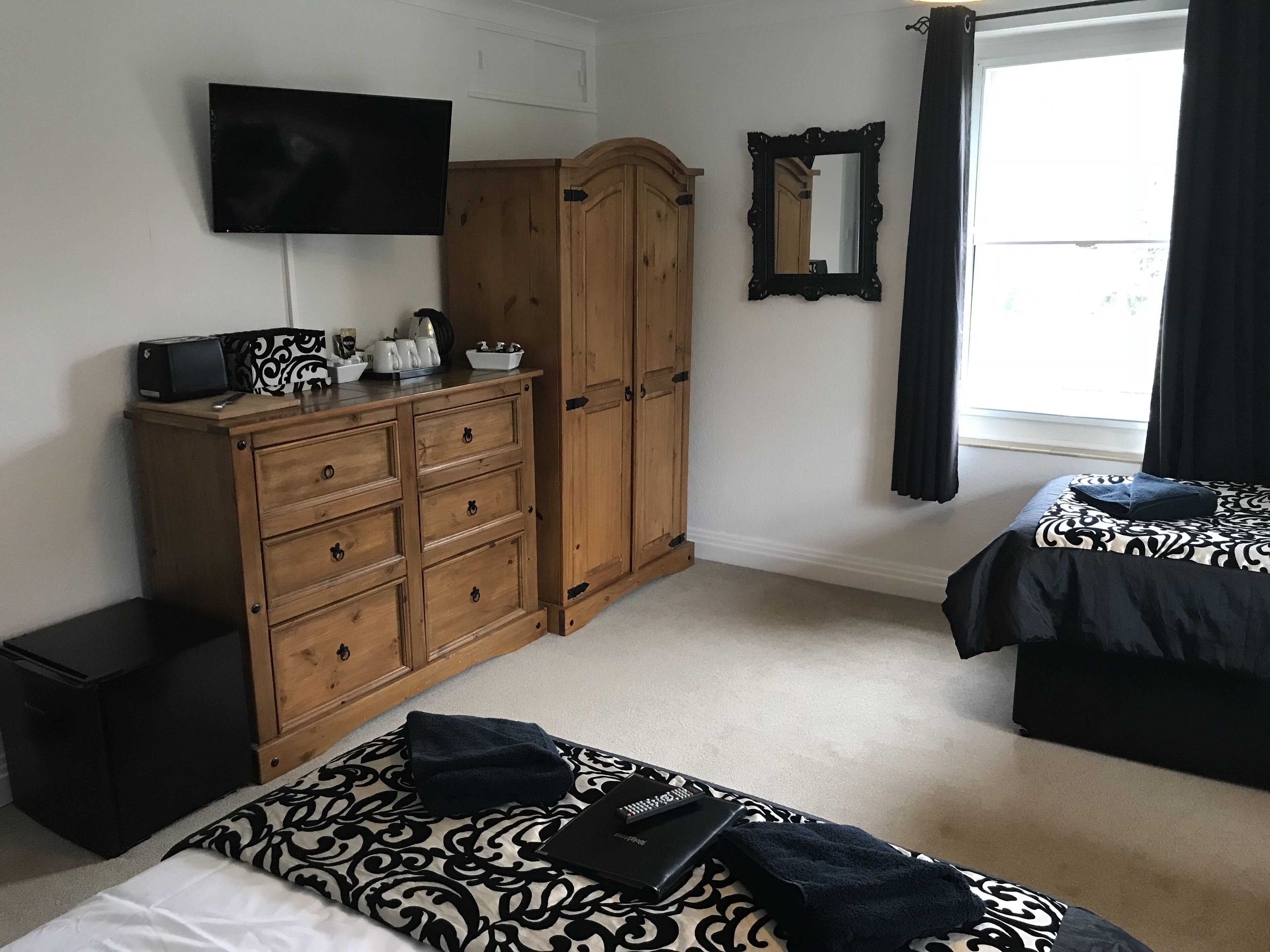 Une chambre avec deux lits, une armoire en bois, un téléviseur à écran plat, un miroir et une fenêtre avec des rideaux.