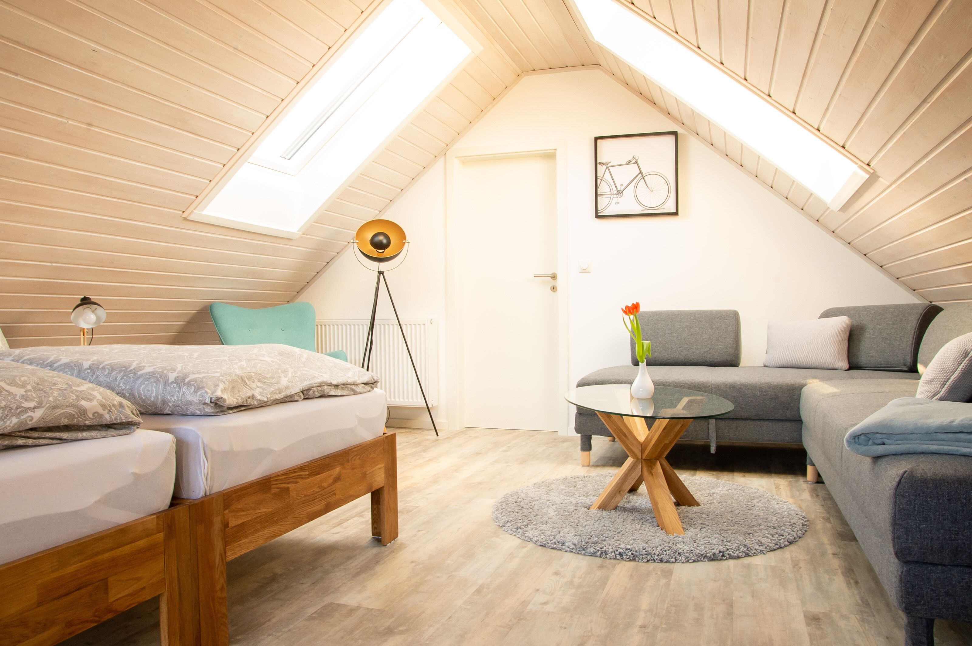 Ett mysigt sovrum på vinden med en säng, en soffa, ett litet runt bord och en golvlampa.