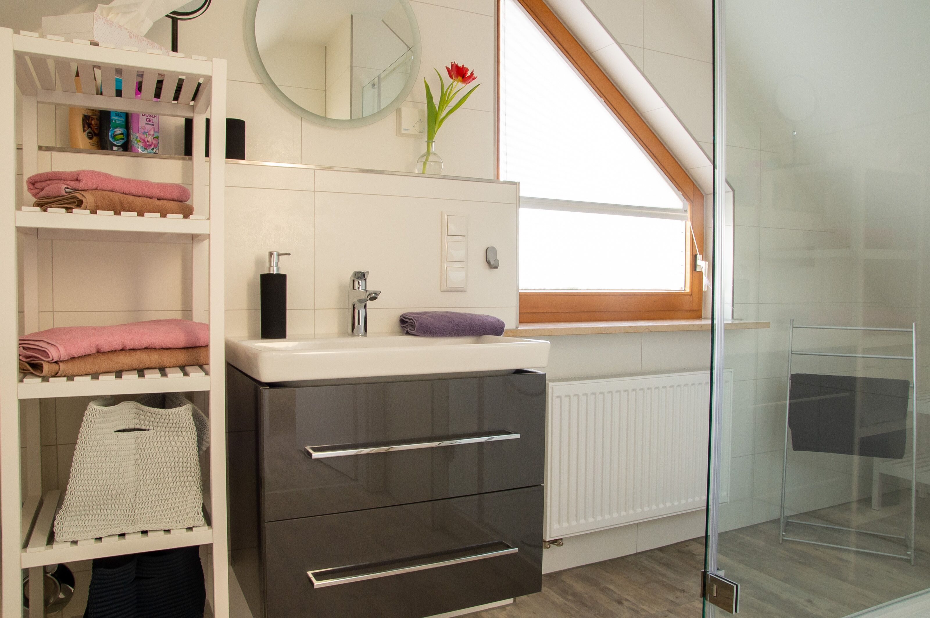A modern bathroom with a white vanity, a glass shower enclosure, and a skylight.